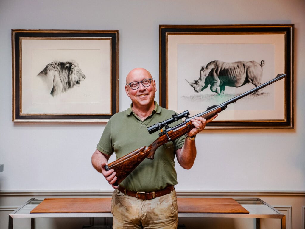 Ralph Paschen mit Gewehr vor Tierbildern im Jagdhaus Wilhelmshöhe.